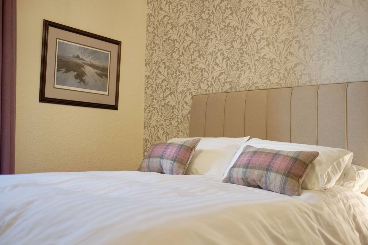 Une chambre d’hôtel avec un lit, deux oreillers, un tableau encadré au mur et un papier peint à motifs.