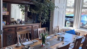 A dining room with a wooden table set for four, surrounded by chairs. A large mirror and a potted plant are visible. - Ravenswood Guest House (Stirling)