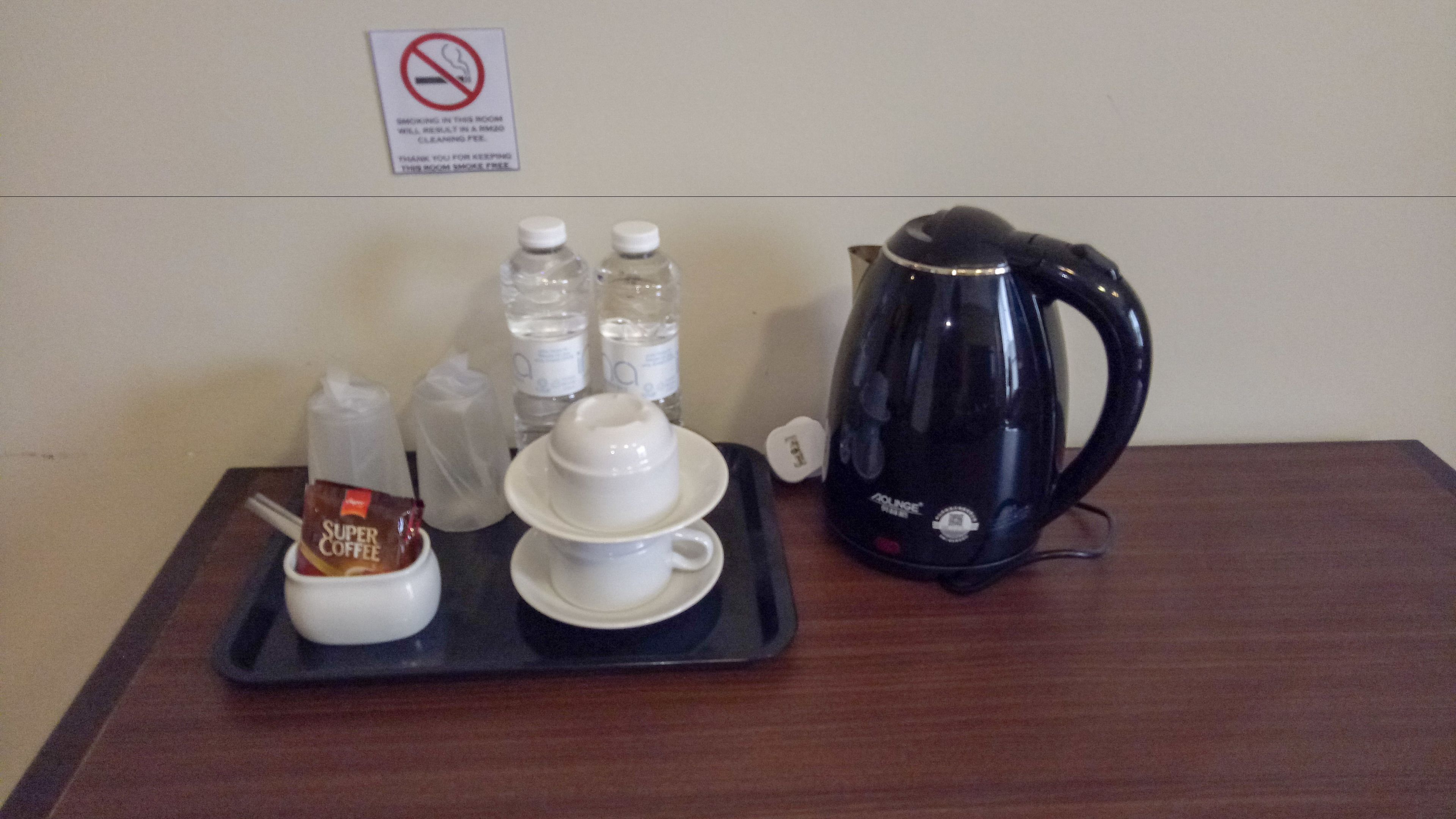 A tray with a coffee pot, cups, and bottled water on a wooden table.