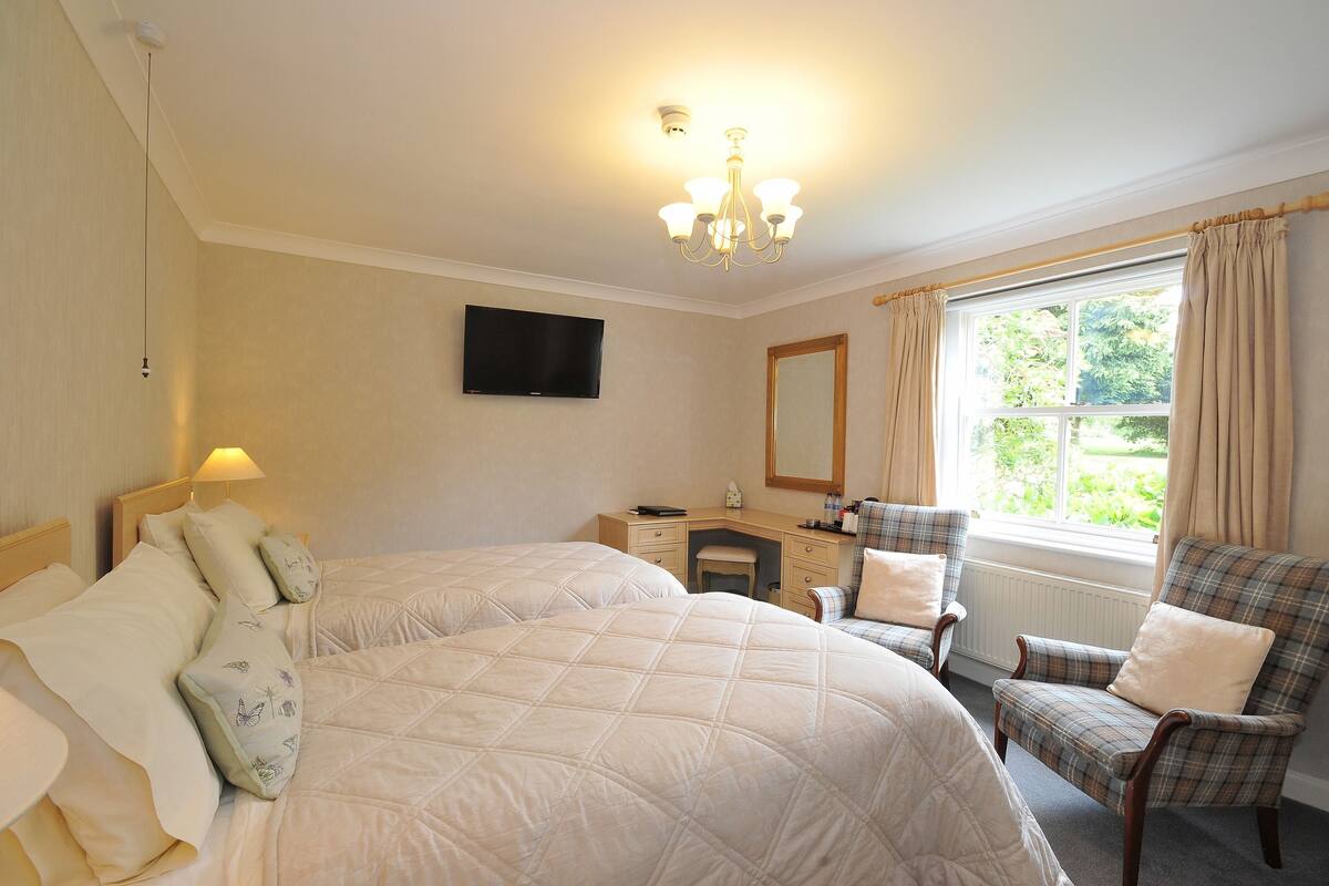 Een slaapkamer met twee bedden, een bureau, een stoel, een televisie en een raam met gordijnen.
