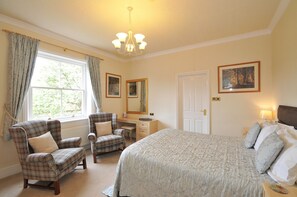 A bedroom with a large bed, two chairs, a dresser, and a window with curtains. - Marton Grange Country House (Bridlington)