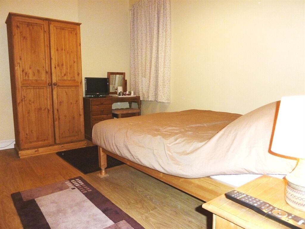 A bedroom with a bed, wooden wardrobe, bedside table, and a remote control.