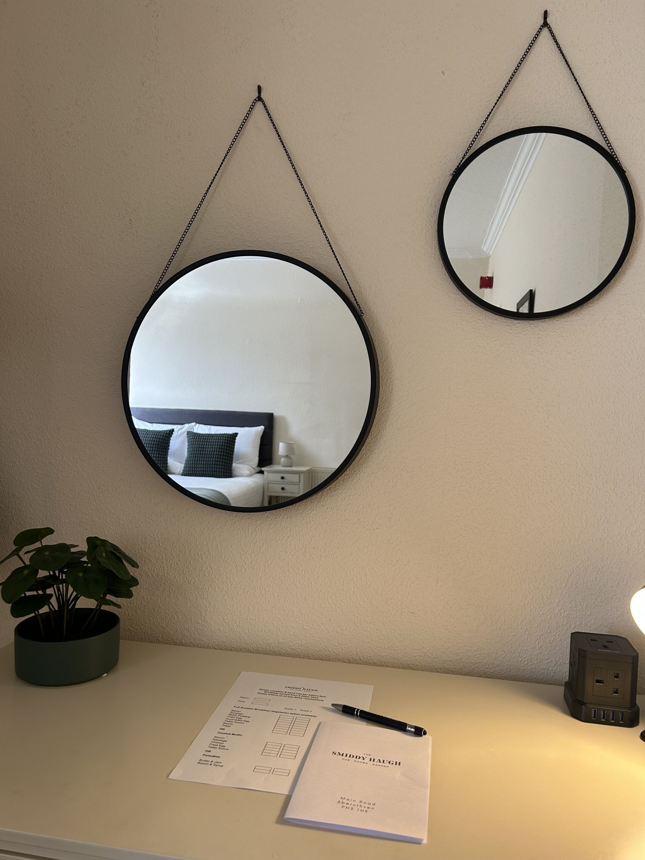 Two round mirrors on a wall, a potted plant, a notepad, a pen, and a power outlet.