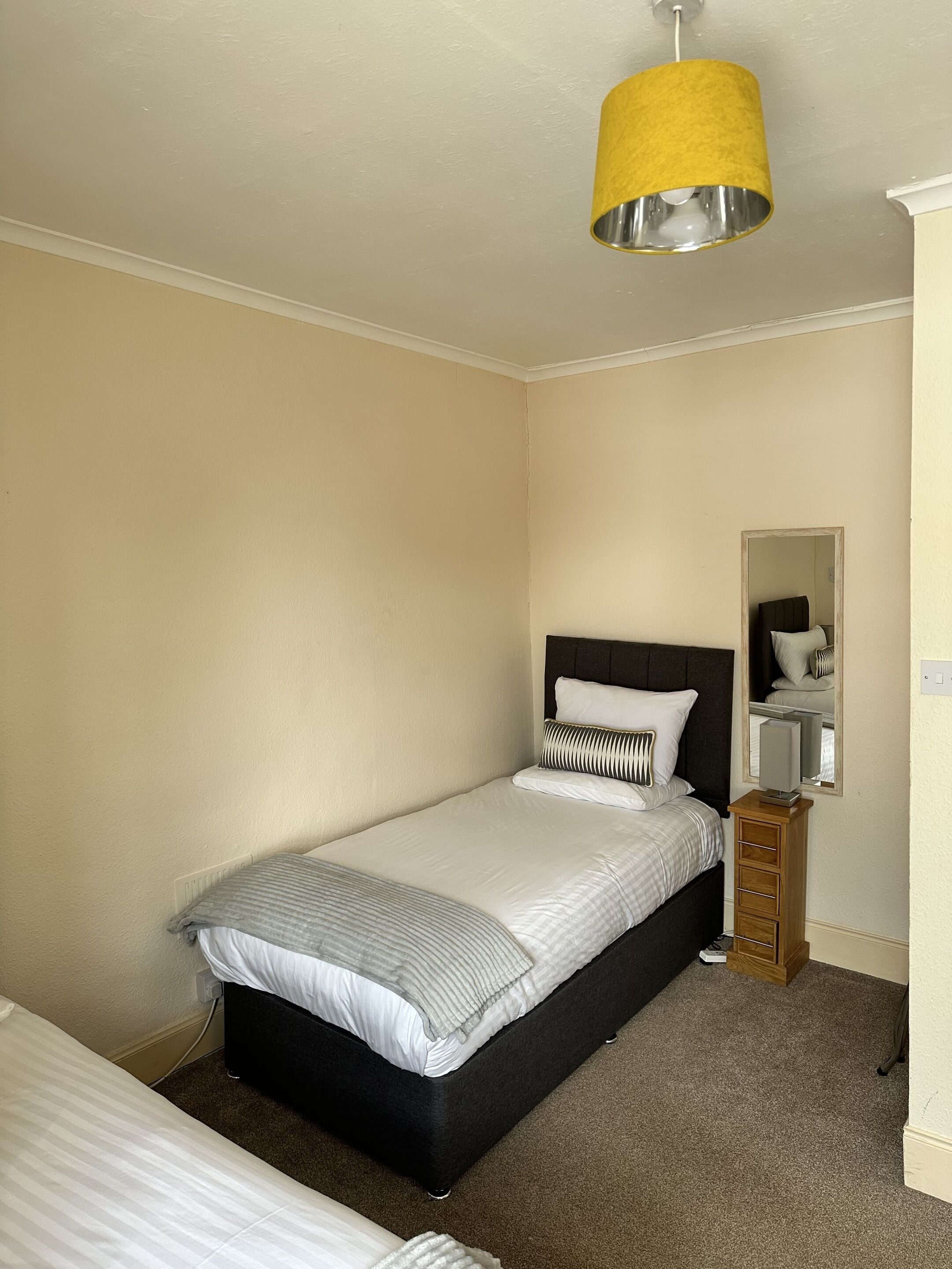 A bedroom with a single bed, a bedside table, a mirror, and a hanging lamp.