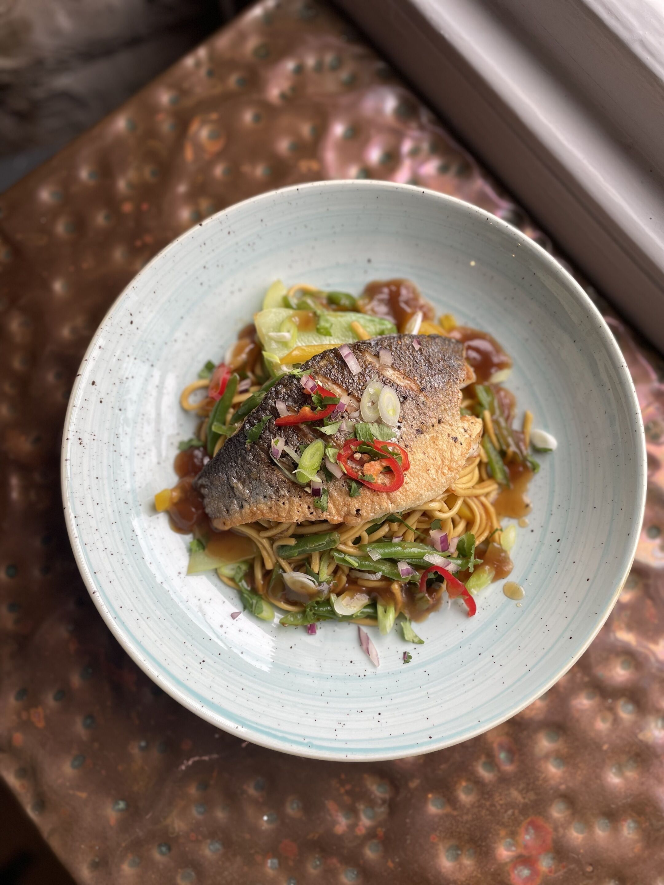 Une assiette de nourriture comprenant du poisson, des nouilles et des légumes.