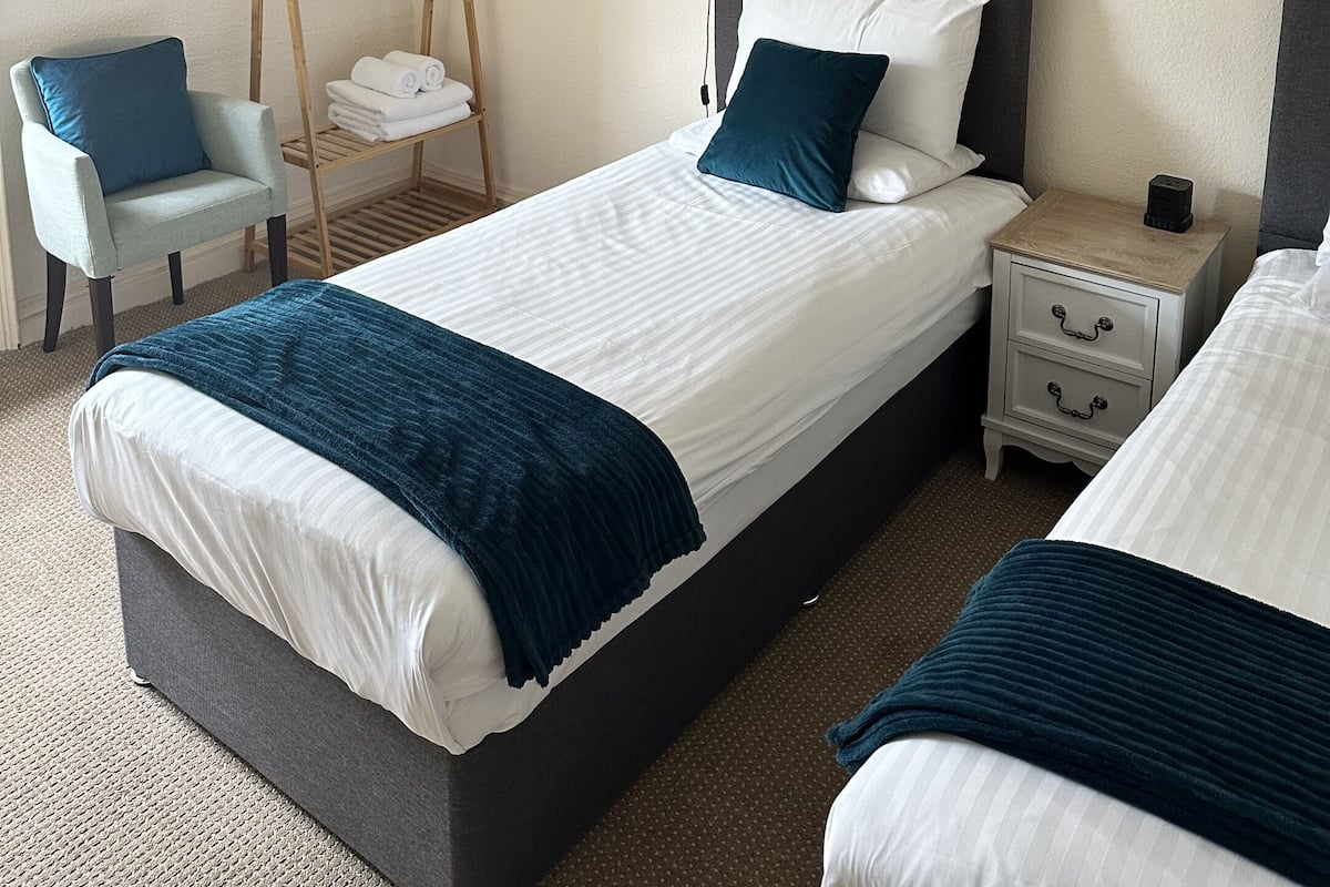 A neatly arranged bedroom with a bed, bedside tables, a hanging light fixture, a chair, and a wooden hanger stand.