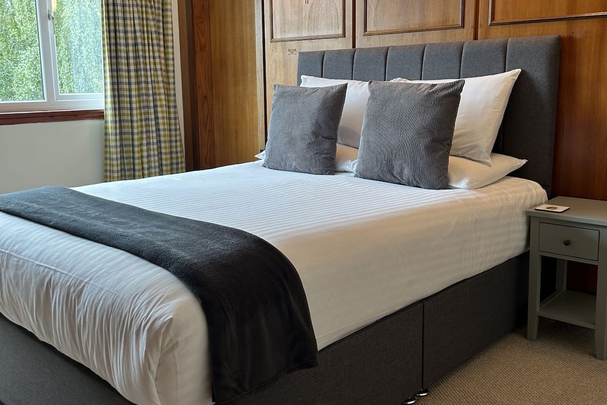 A neatly made bed with a grey headboard, a bedside table, and a window with curtains.