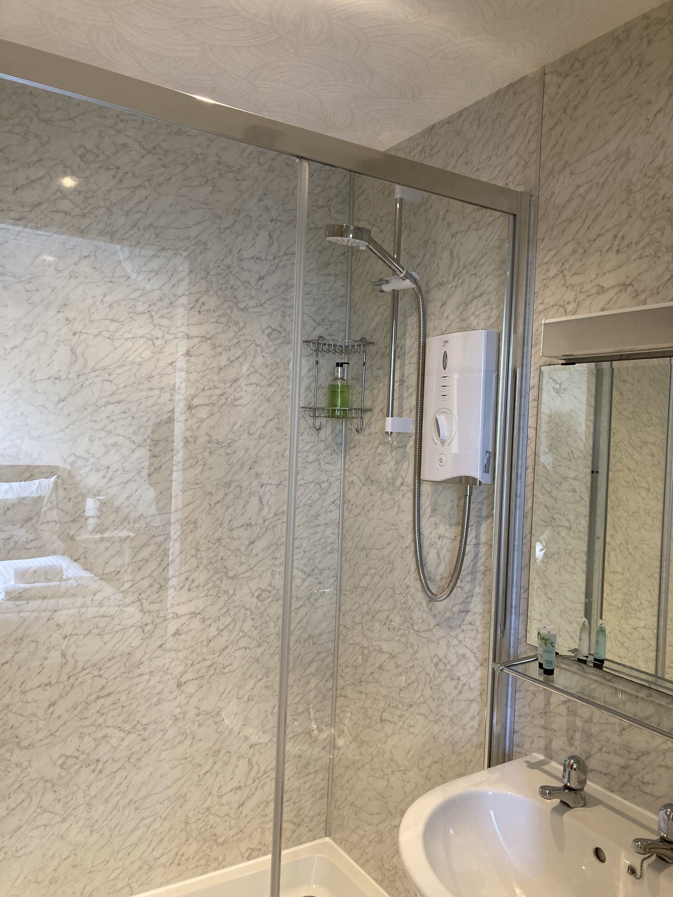 A modern bathroom with a glass-enclosed shower, a white sink, and marble walls.