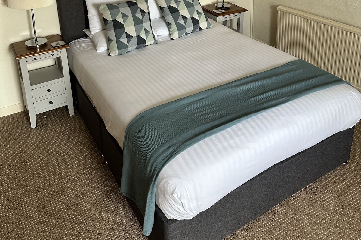 A neatly made bed with a dark headboard, two bedside tables with lamps, a wall-mounted artwork, and a radiator.
