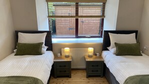 A twin room with two beds, each with a nightstand, a lamp, and a window with blinds. - Smiddy Haugh (Auchterarder)