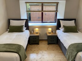 Habitación doble con dos camas, cada una con una mesita de noche, una lámpara y una ventana con persianas.