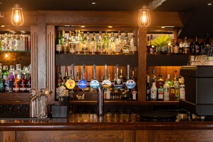 Un bar con múltiples grifos, estantes llenos de botellas de licor y una escultura decorativa de metal.