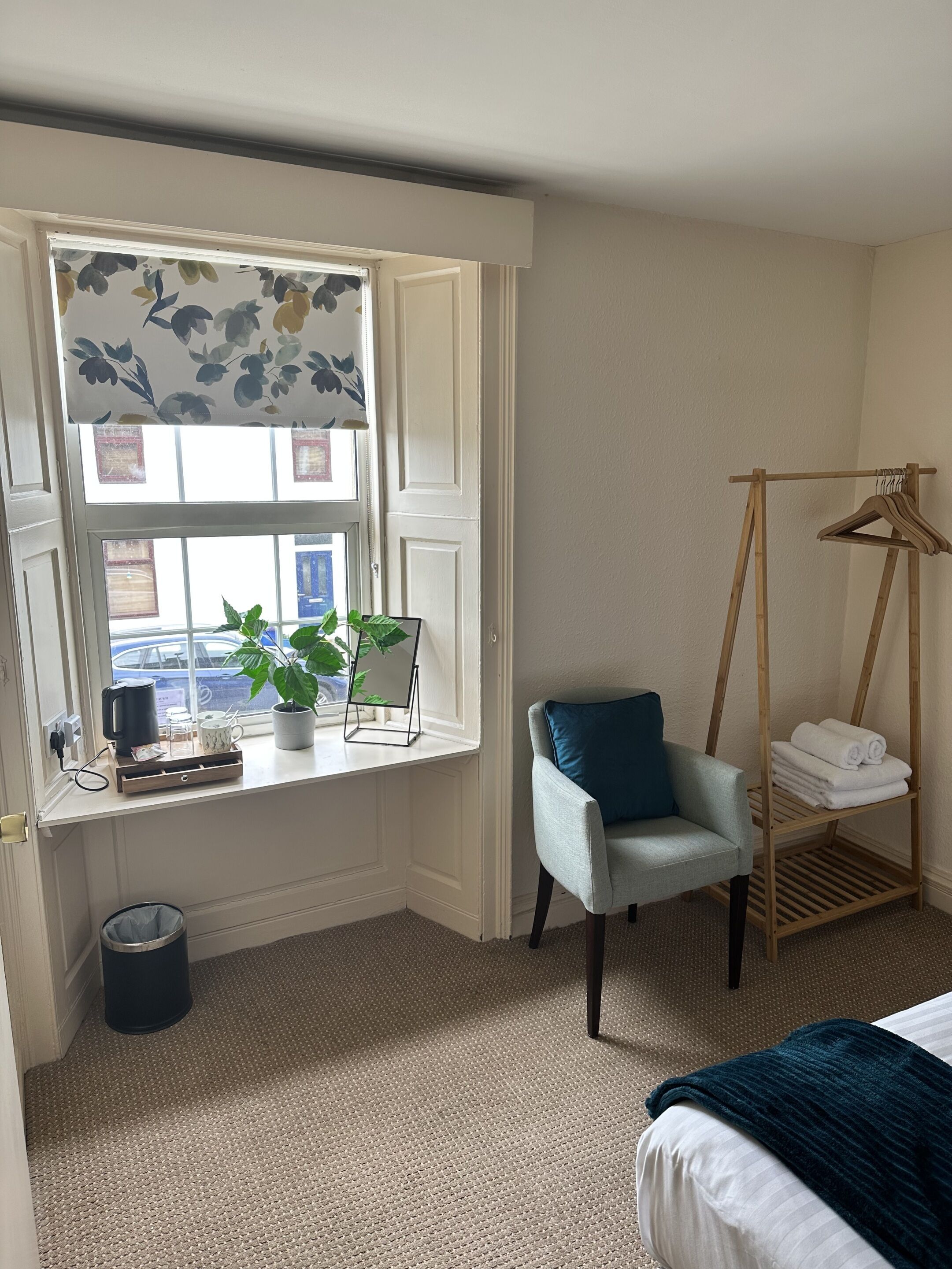Une chambre avec une fenêtre, une chaise, un cintre en bois et un lit.