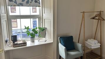 Une chambre avec une fenêtre, une chaise, un cintre en bois et un lit.