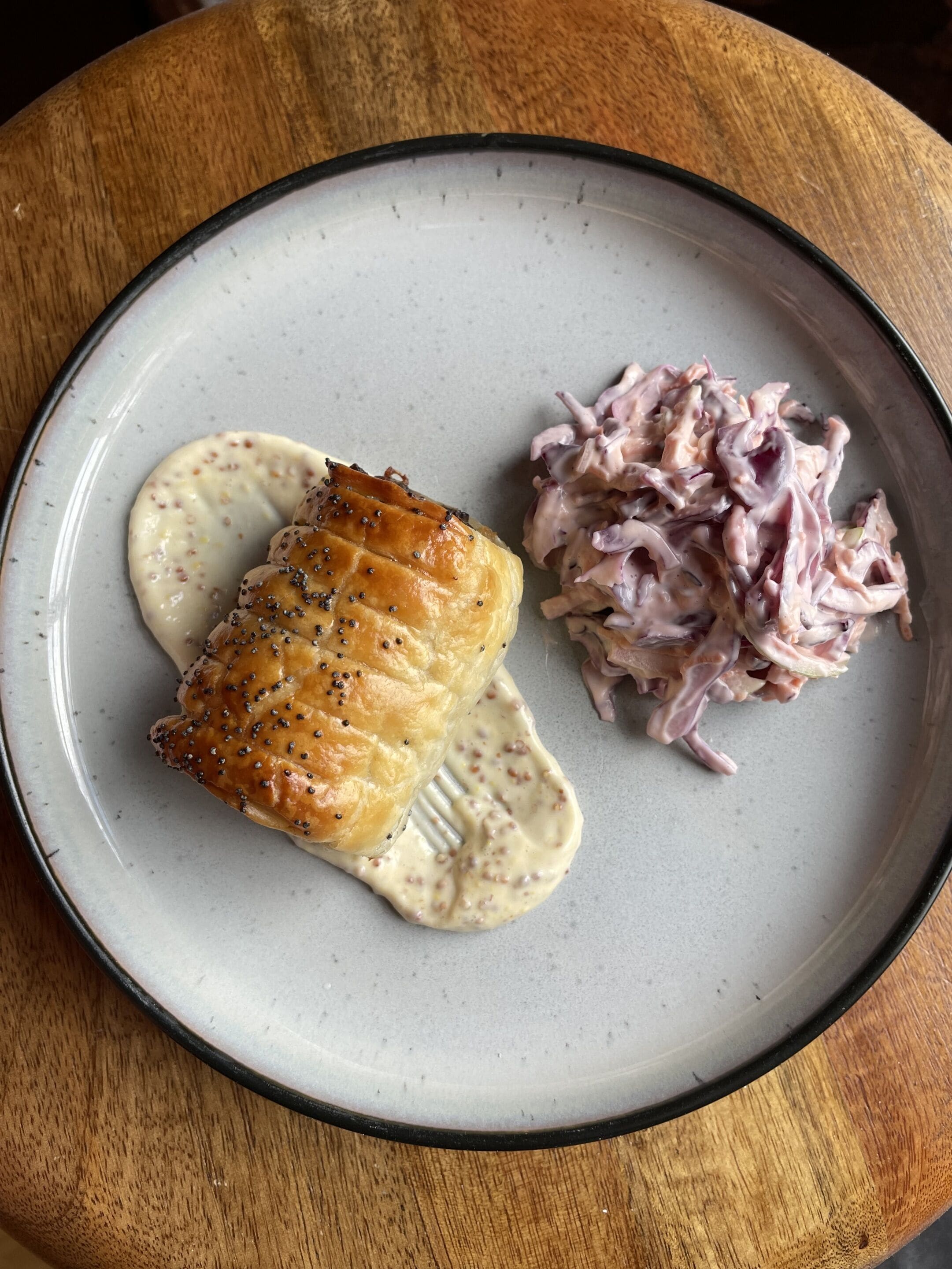 A plate with a piece of salmon, a creamy sauce, and a side of pickled vegetables.