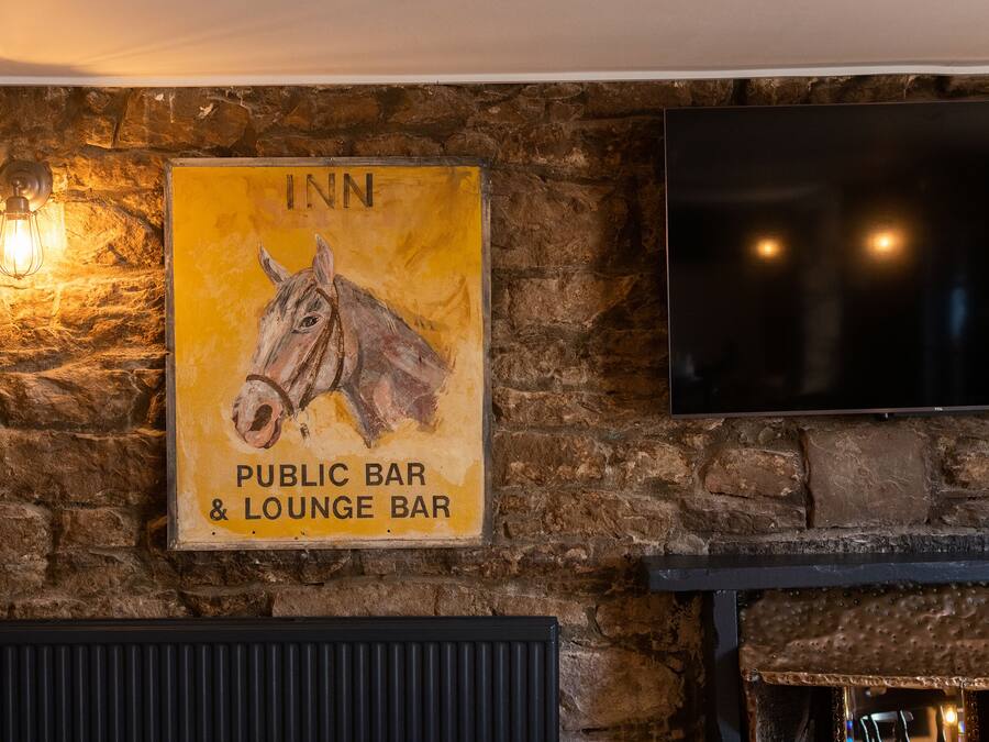 A wall with a sign for a public bar and lounge bar, a mounted television, and a stone wall.