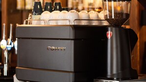 A coffee machine with a glass hopper filled with coffee beans, a branded logo, and a wooden counter. - Smiddy Haugh (Auchterarder)