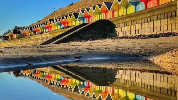 A beach with colorful beach huts and a clear reflection in the water. - St Michael's Guest House (Scarborough)