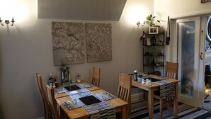 A dining area with a wooden table and chairs, a striped table runner, and wall-mounted artwork. - St Michael's Guest House (Scarborough)