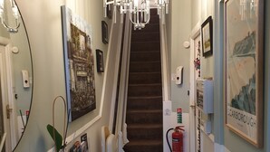 A hallway with a carpeted staircase, a chandelier, framed artwork, a fire extinguisher, and a small table with a potted plant. - St Michael's Guest House (Scarborough)