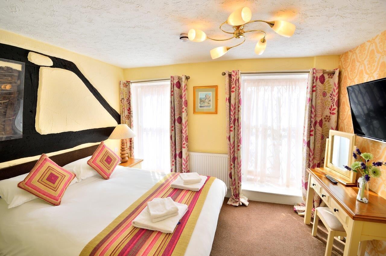 A hotel room with a large bed, a desk with a mirror, and a television.