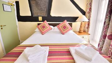 A hotel room with a bed, pillows, a lamp, a window with curtains, and a door.