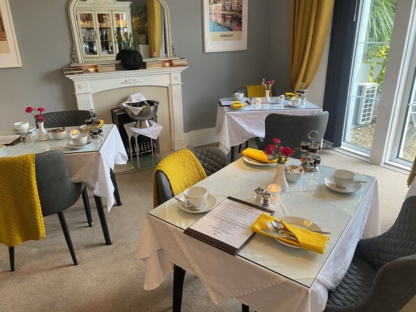 Un espace repas avec des tables dressées pour le repas, une cheminée et une vue sur l’extérieur.