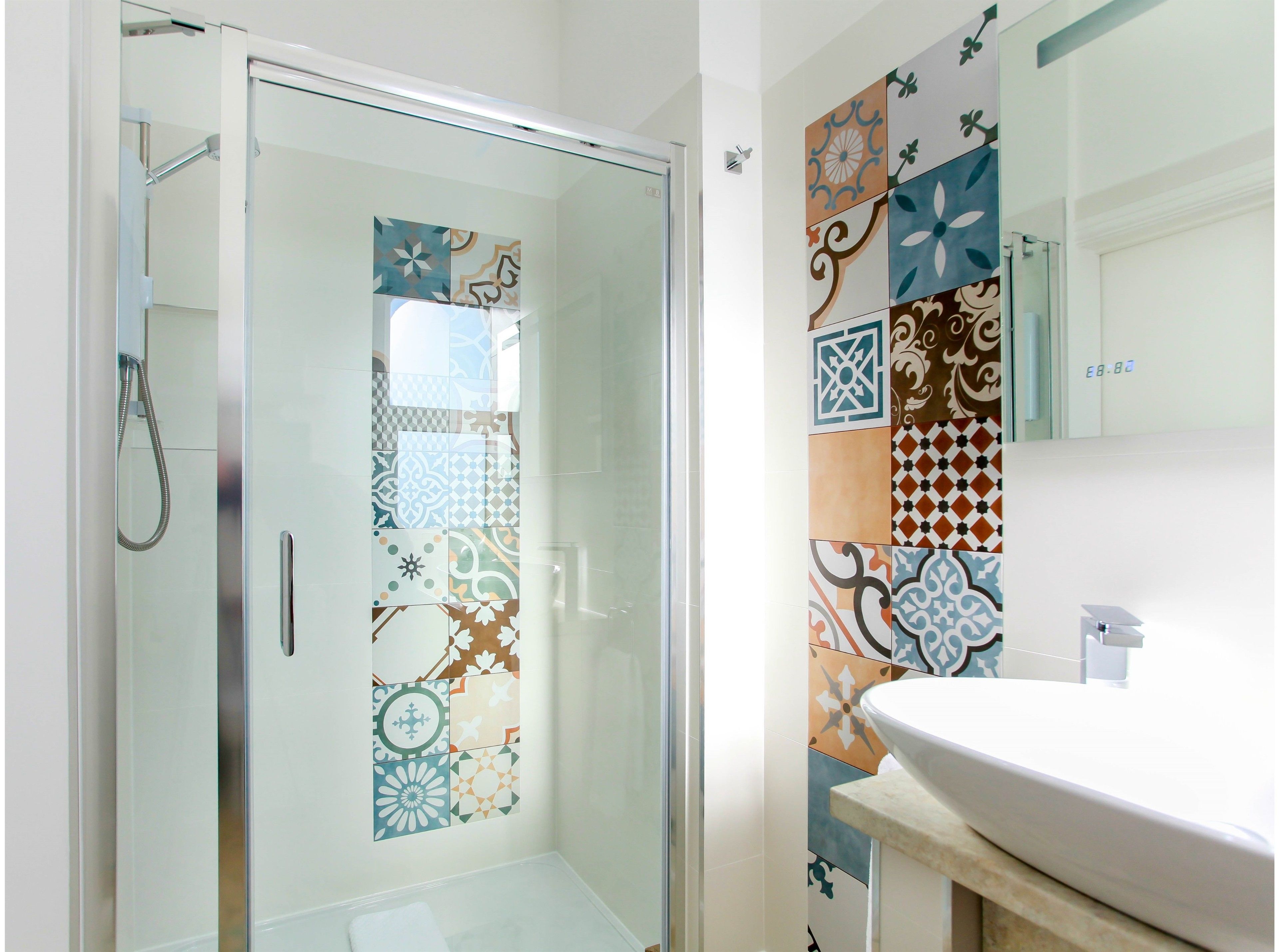 Un baño con mampara de vidrio, lavabo y pared decorada con baldosas estampadas.