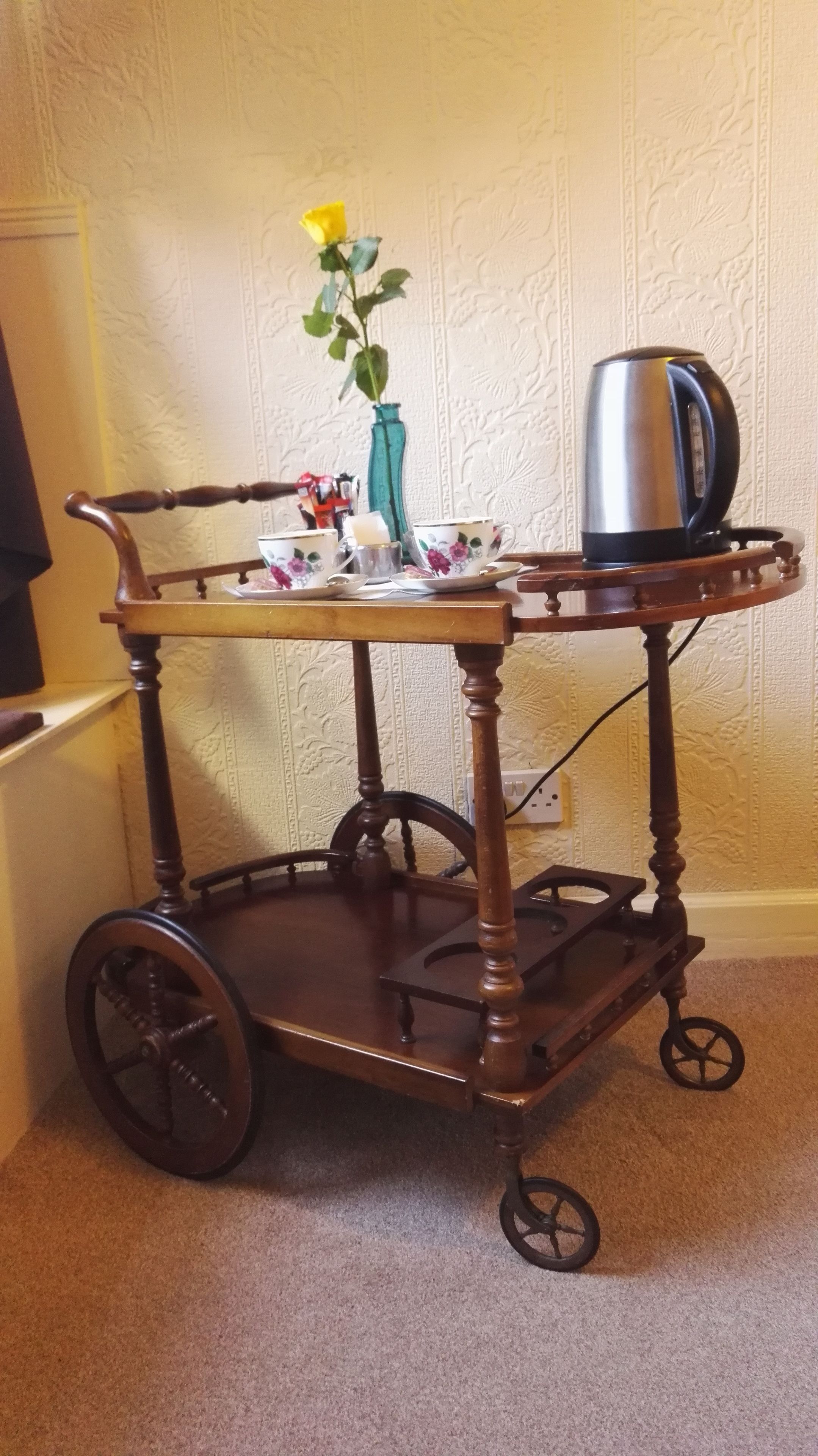 A wooden cart with wheels, a vase with a yellow flower, and a kettle.