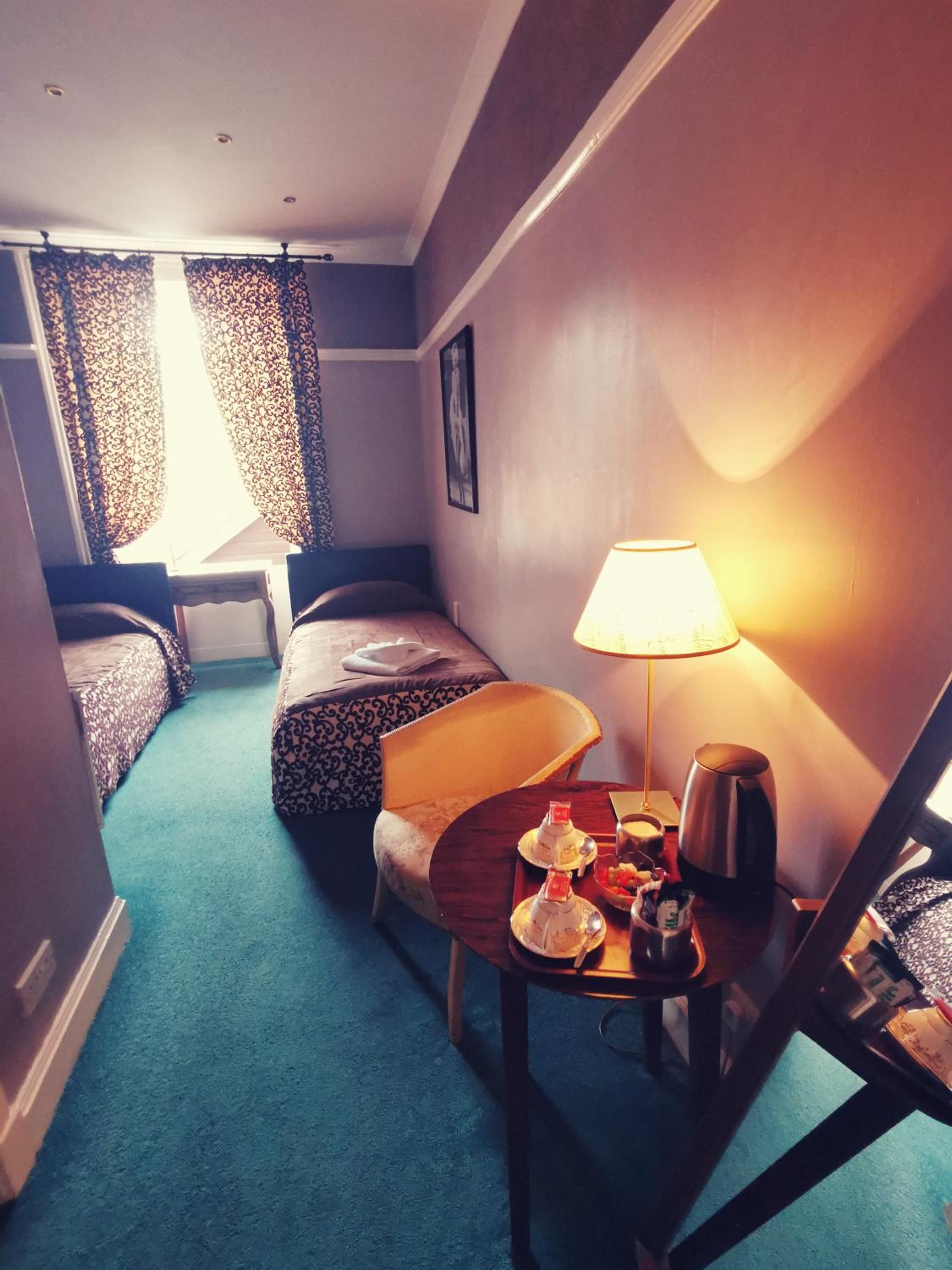 Ett hotellrum med en säng, en stol, ett bord med en lampa och en kaffebryggare.