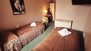 Ein Hotelzimmer mit zwei Einzelbetten, einem Schreibtisch mit Stuhl, einer Lampe, einem Fernseher und einem gerahmten Bild an der Wand.