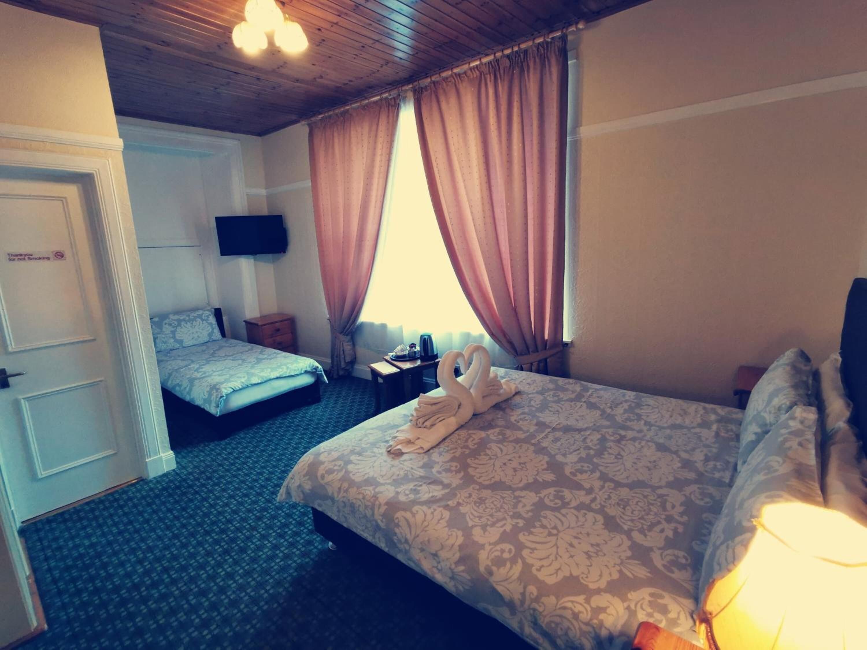 Habitació d'hotel amb dos llits, una televisió de pantalla plana, una taula de nit i una finestra amb cortines.