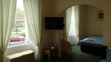 A hotel room with a bed, a desk, a chair, a television, and a window with curtains.