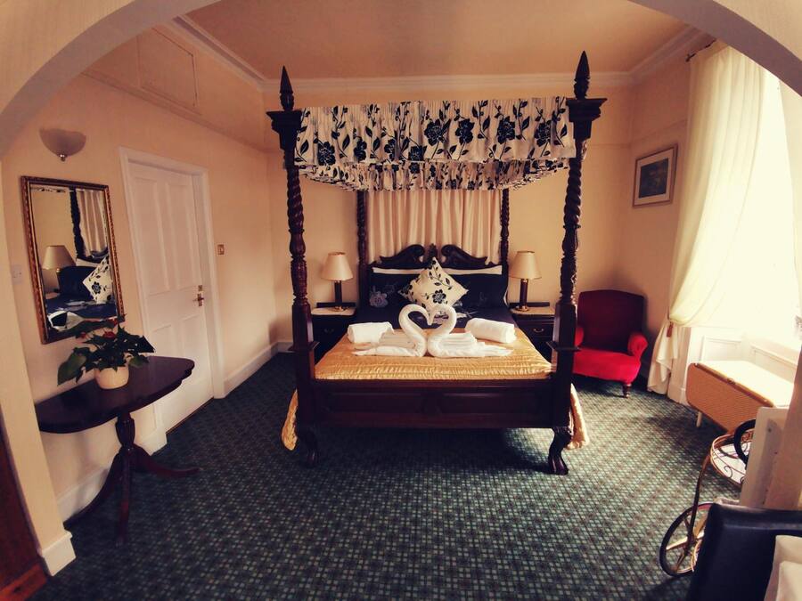 A four-poster bed with a canopy, a bedside table with a lamp, a red armchair, and a mirror on the wall.