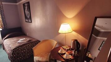 Una habitación de hotel con una cama, una silla, una mesa con lámpara y un refrigerador.