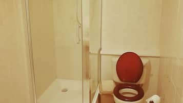 A bathroom with a glass-enclosed shower, a toilet with a red seat, and a white mat on the floor.