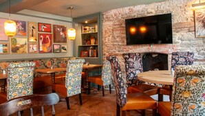 A restaurant interior with wooden furniture, a brick wall, and a flat-screen TV mounted above a fireplace. - George Inn, Mere (Warminster)