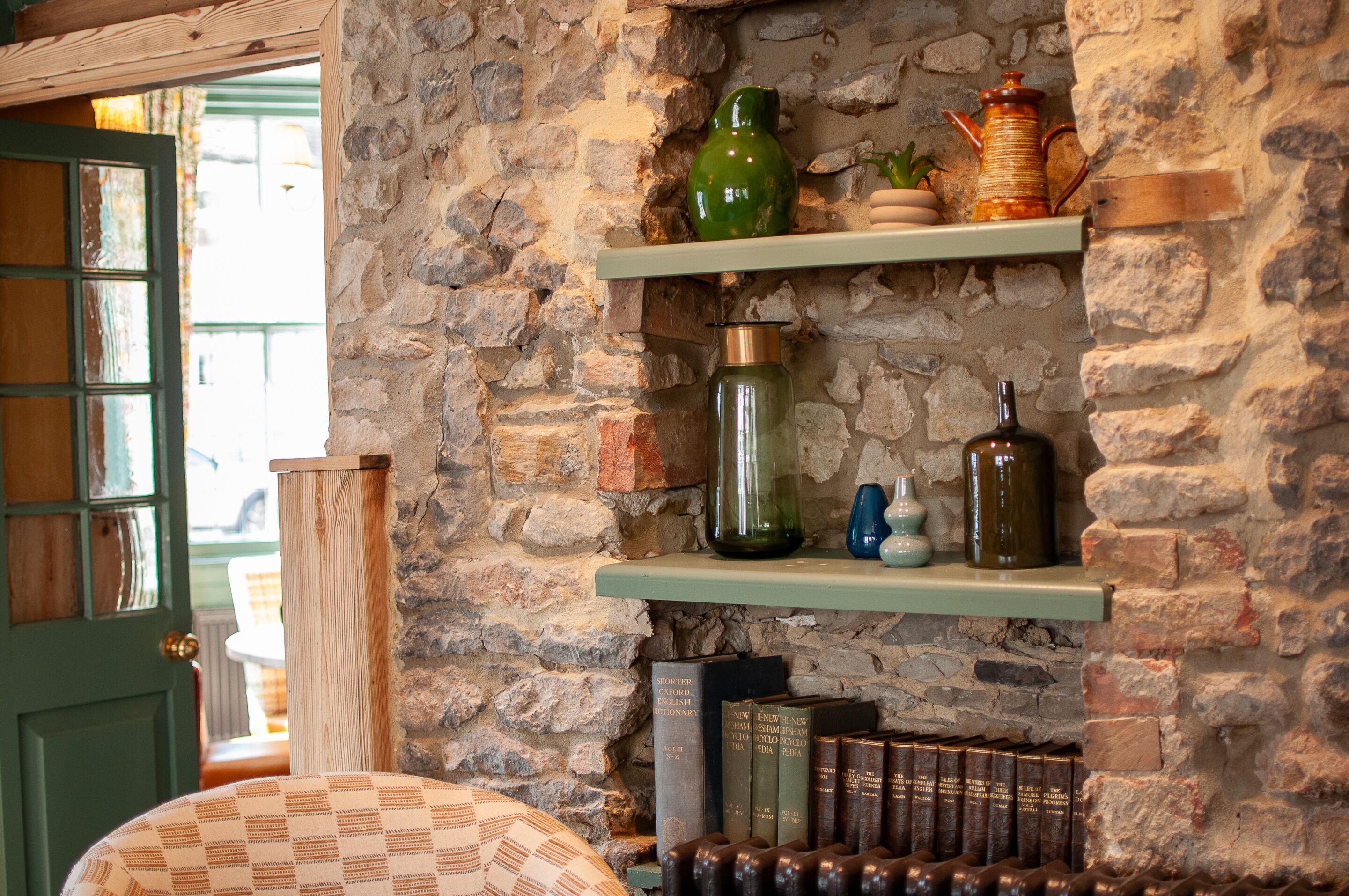 Una habitación con pared de piedra, estantes de madera y una colección de libros.