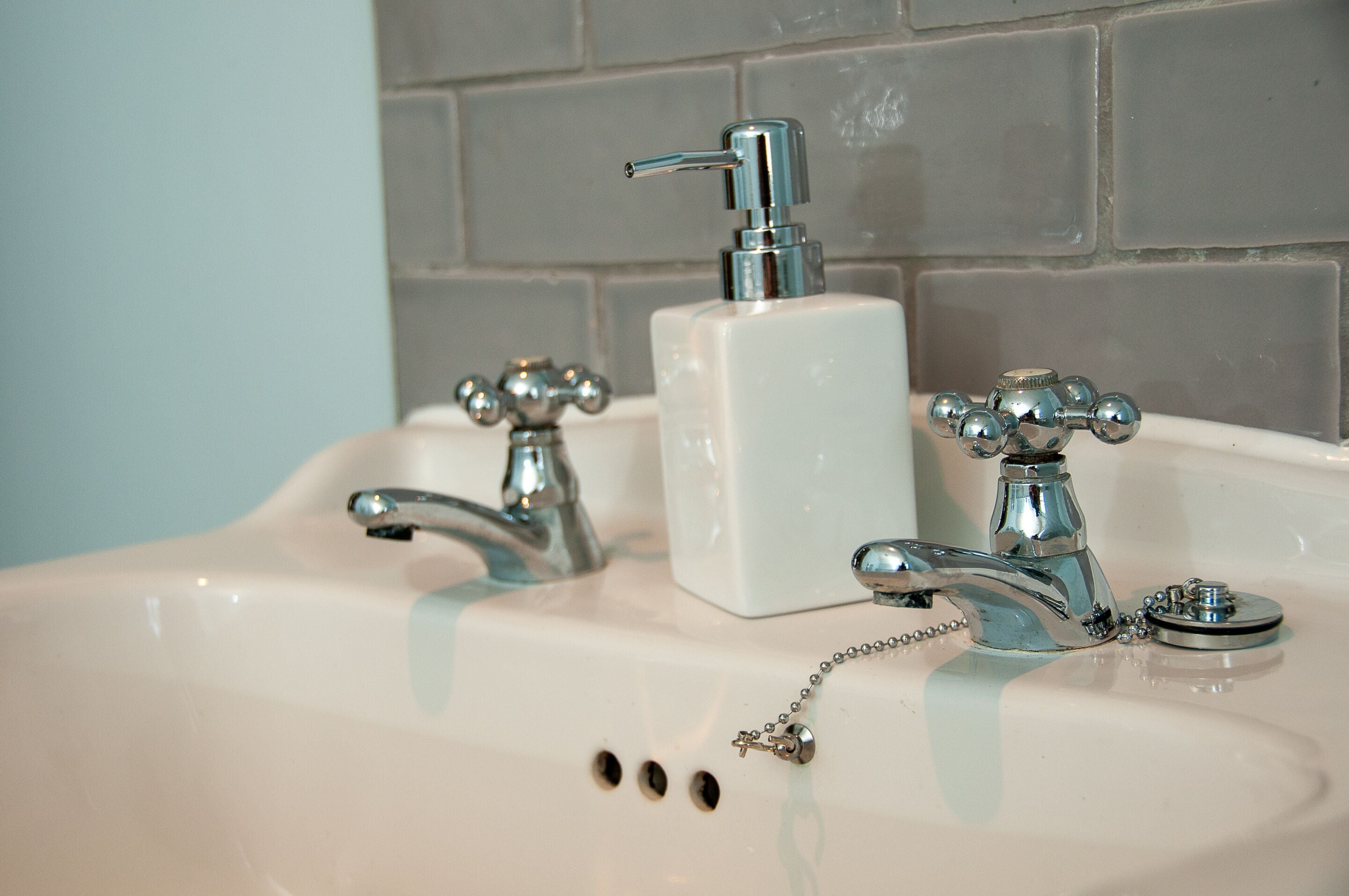 A bathroom sink with two faucets and a soap dispenser.