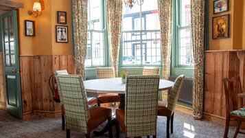 Un comedor con una mesa redonda y cuatro sillas, rodeado de paredes cubiertas de paneles verdes y una ventana con cortinas de flores.