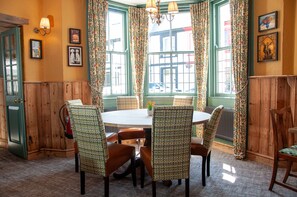 A dining area with a round table and four chairs, surrounded by green paneled walls and a window with floral curtains.