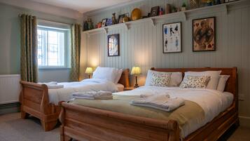A hotel room with two wooden beds, a window with curtains, and a shelf with various decorative items.