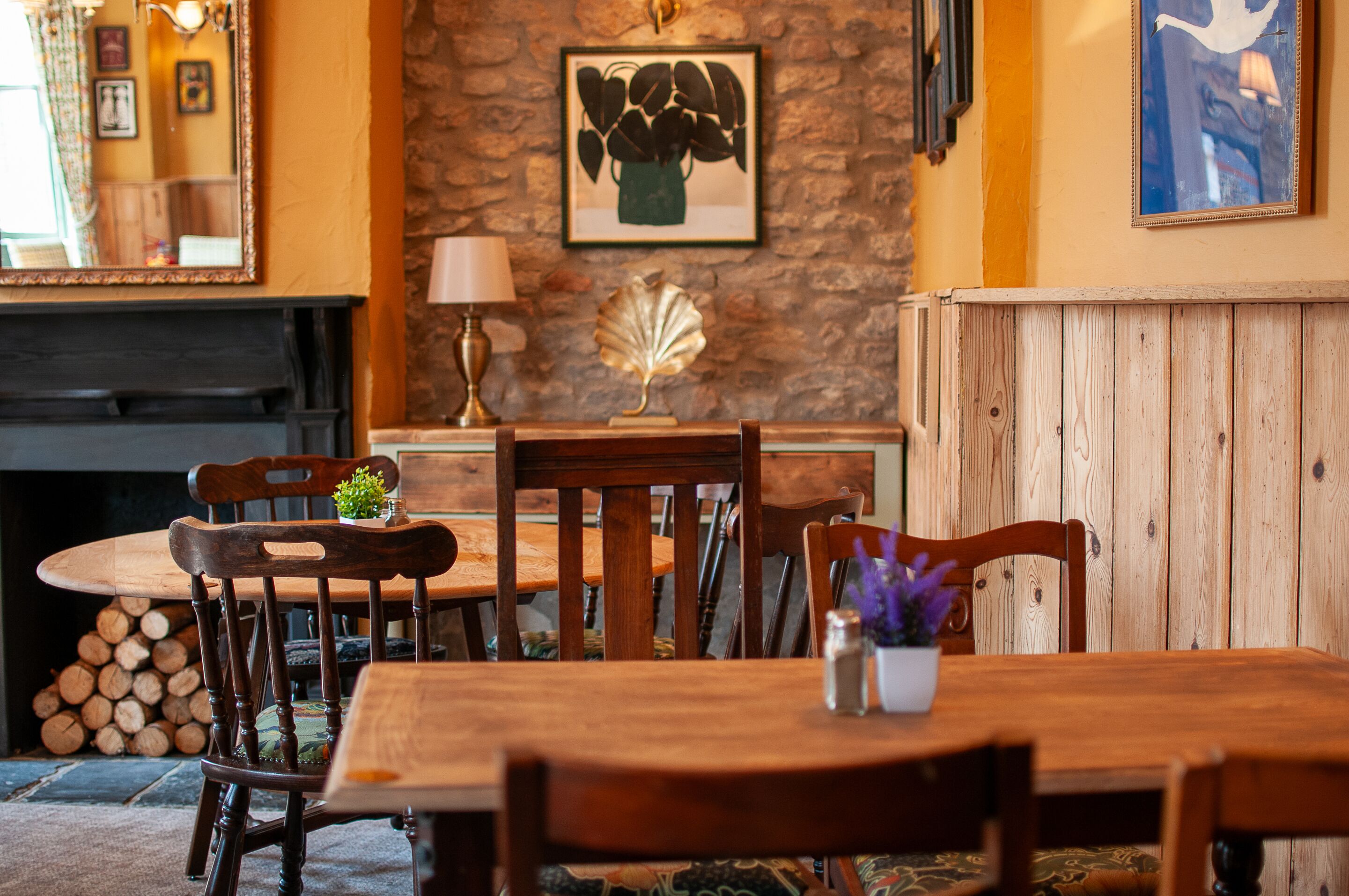 Un comedor con una mesa y sillas de madera, una chimenea y una pared de piedra con una obra de arte enmarcada.