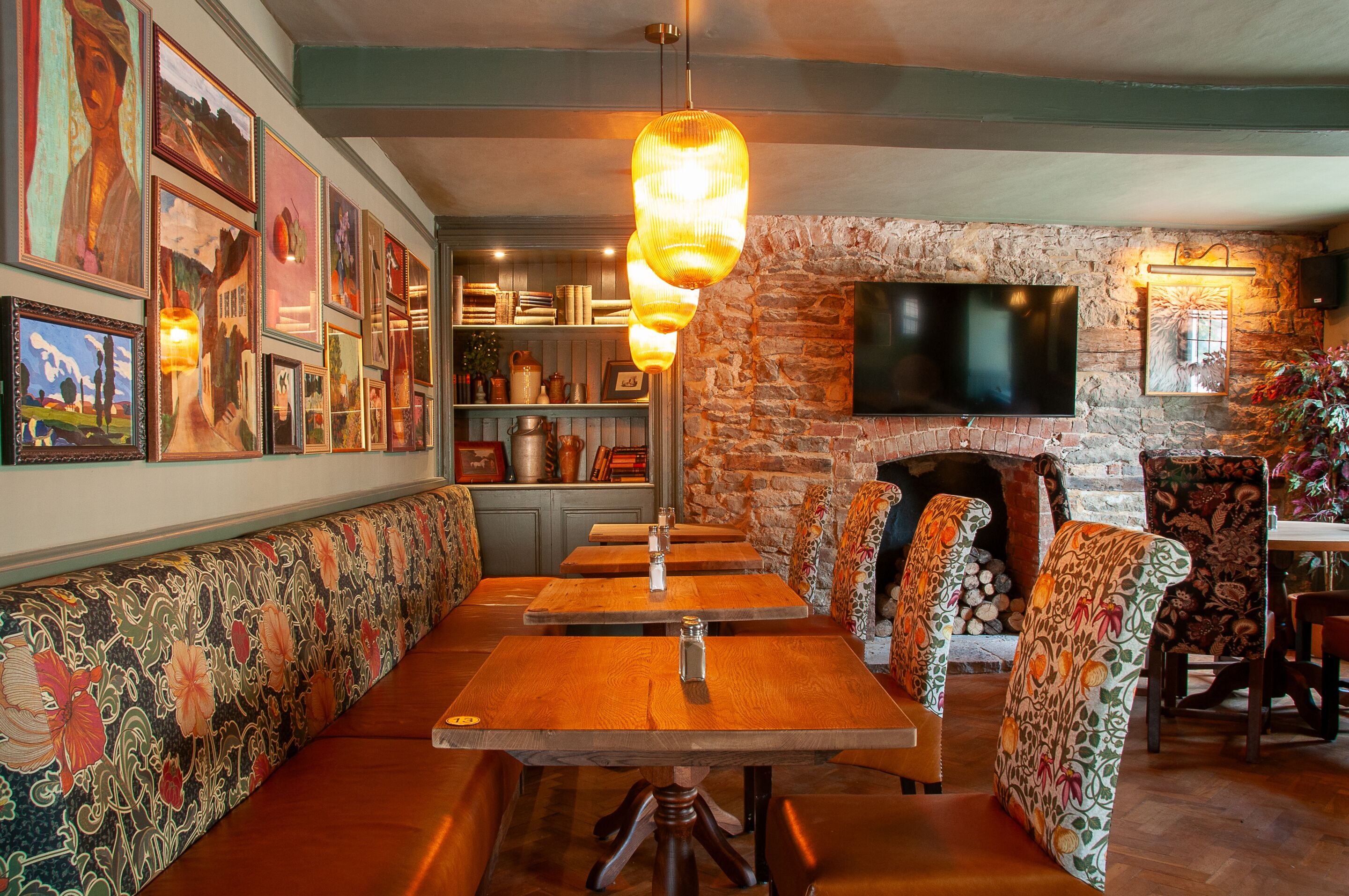 A restaurant interior with wooden benches and tables, a stone wall, and a flat-screen TV mounted on the wall.