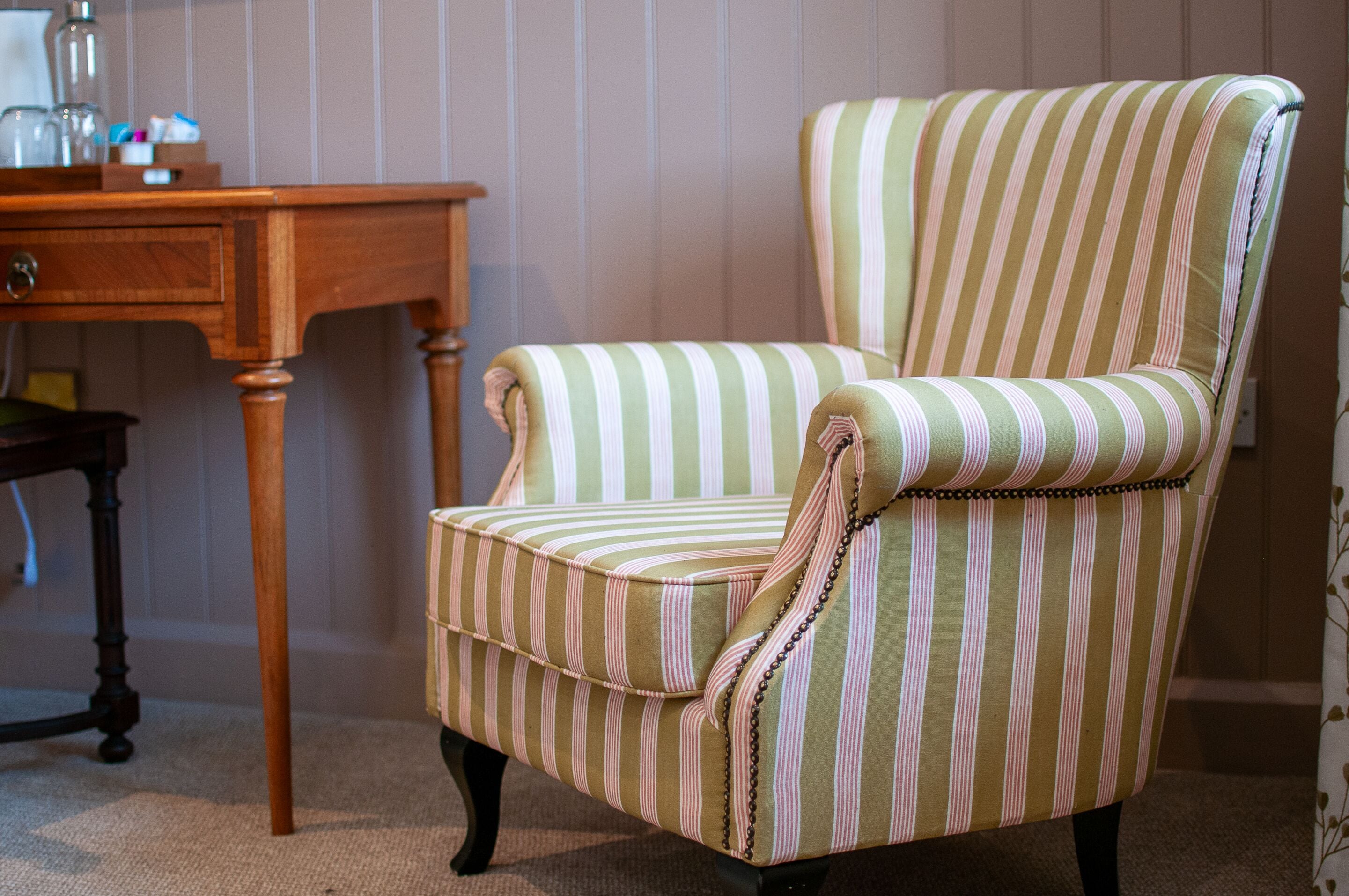 Un sillón a rayas con una mesa de madera y un escritorio pequeño al fondo.