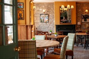 A cozy dining area with wooden furniture, a stone wall, and artwork on the walls. - George Inn, Mere (Warminster)