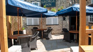 Outdoor seating with umbrellas, a stone building, and a sign reading 'The George Inn'. - George Inn, Mere (Warminster)