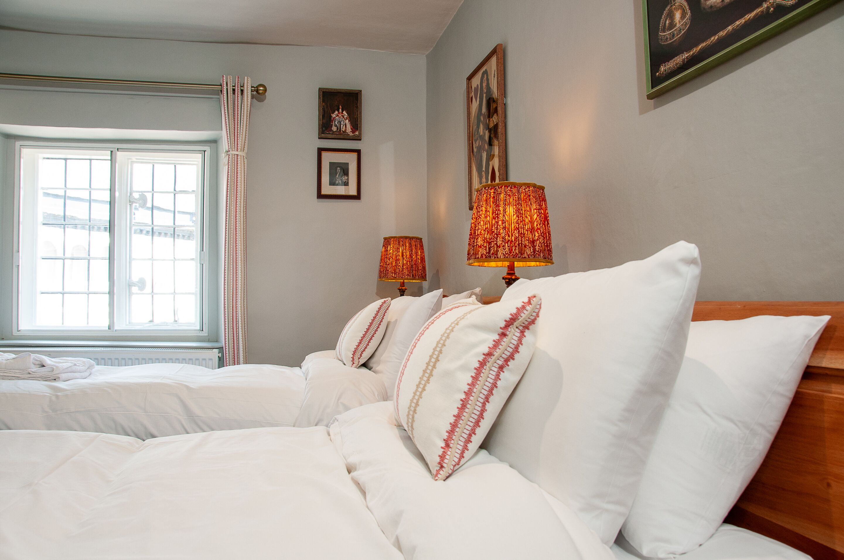 A hotel room with a large bed, two bedside lamps, a window with curtains, and framed pictures on the wall.