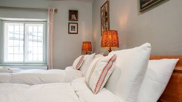 A hotel room with a large bed, two bedside lamps, a window with curtains, and framed pictures on the wall.