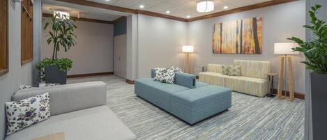 A hotel lobby with a grey sofa, a blue sofa, a small table, and a potted plant.